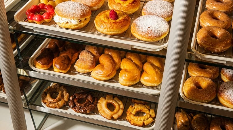 A glass display case filled with various types of donuts, including glazed, powdered, and chocolate.