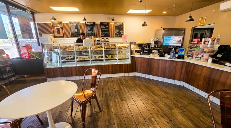 A donut shop interior with a display case full of donuts, a counter, and a customer.